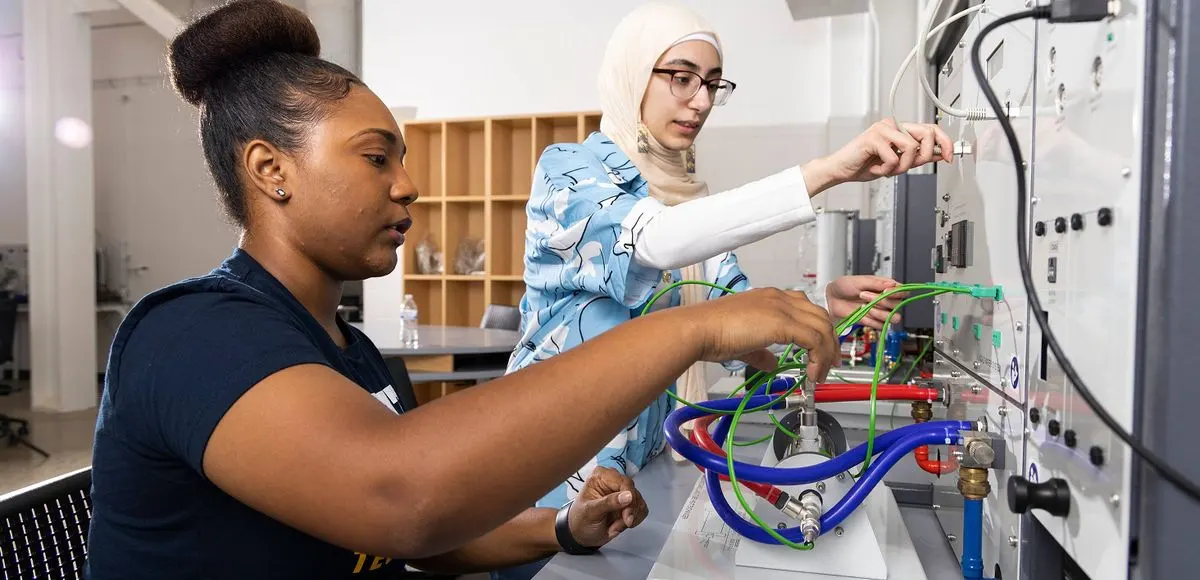 Two people working on equipment involving complex wiring