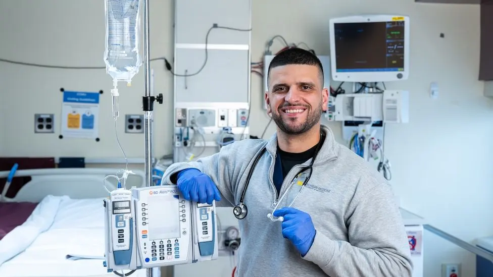 Joshua Truchan with an IV stand in a hospital room