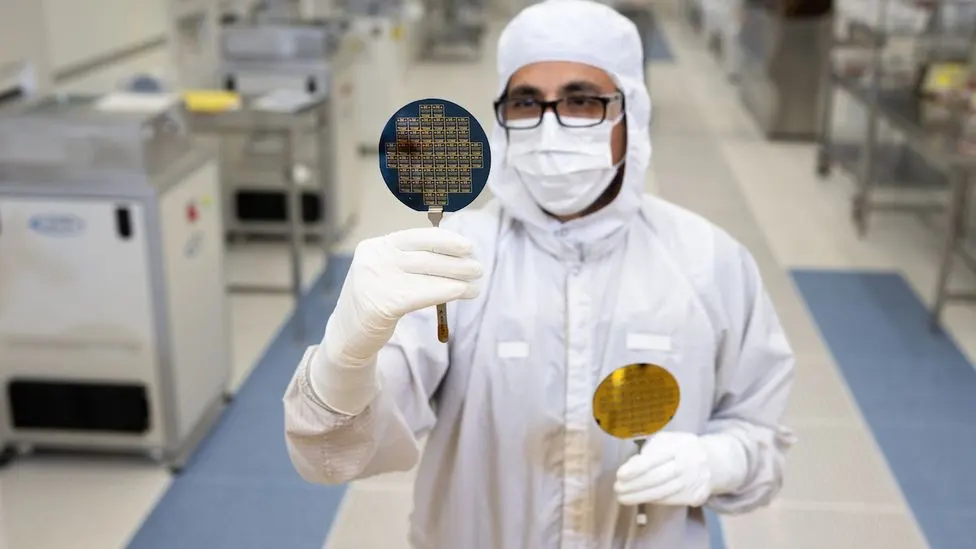 A technician in a cleanroom attire holding a silicon wafer containing microchips