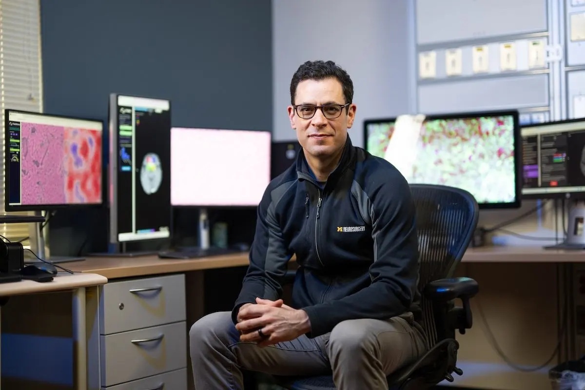Todd C. Hollon, M.D. in a U-M Neurosurgery jacket seated before multiple monitors displaying brain imaging and pathology data