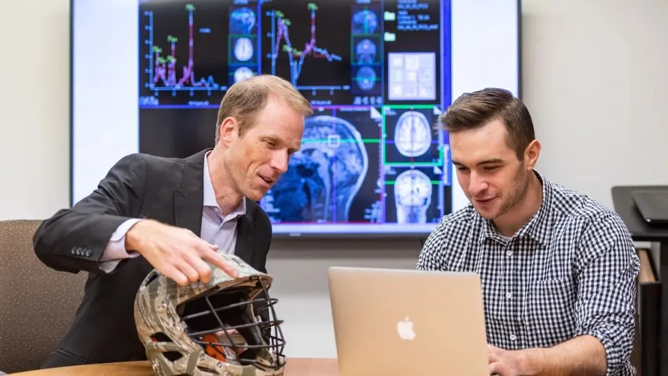 Researchers looking at a helmet and laptop together