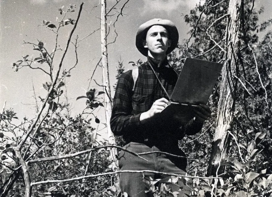 A black and white photo of a researcher taking notes in nature