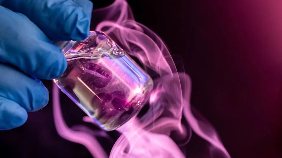 A gloved hand holding a vial with pink gas coming out of it