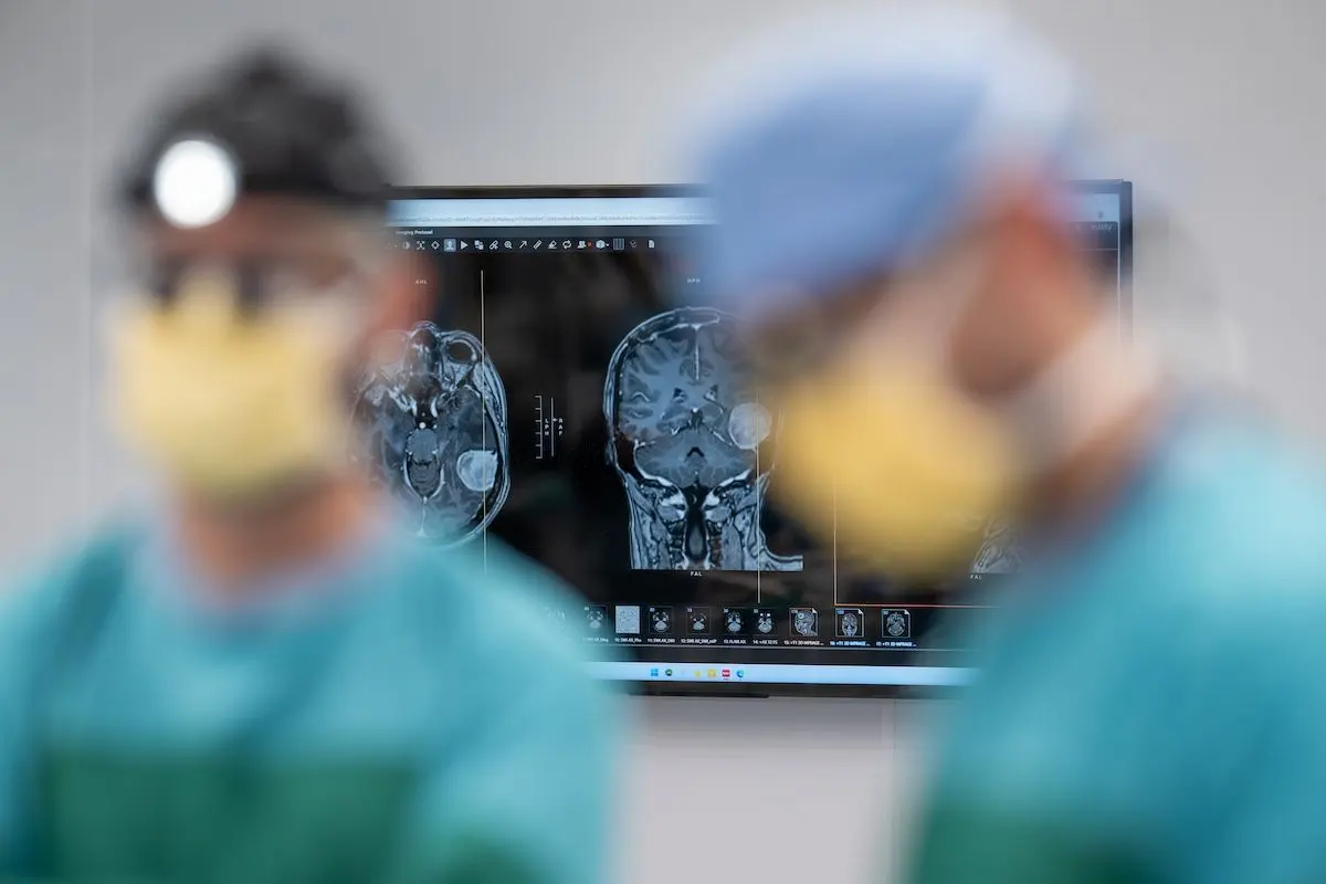 MRI brain scans on a monitor with two blurred surgeons in the foreground
