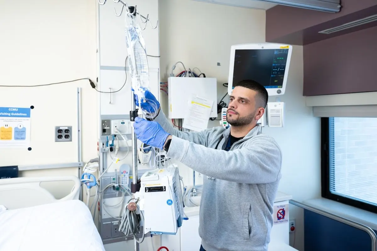Joshua Truchan adjusts an IV bag in a hospital room