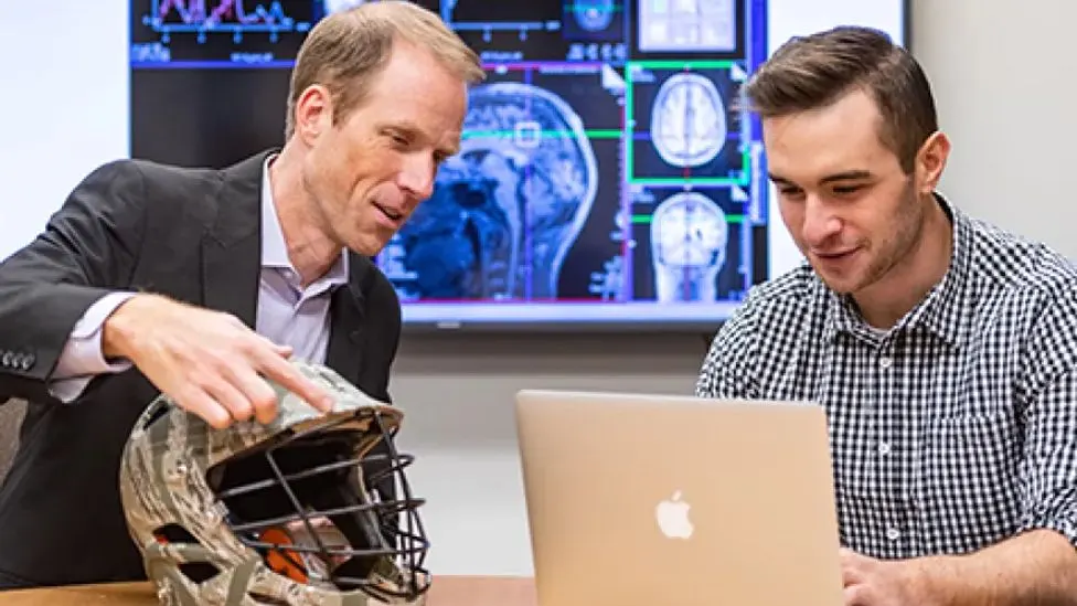 Researchers looking at a helmet and laptop together