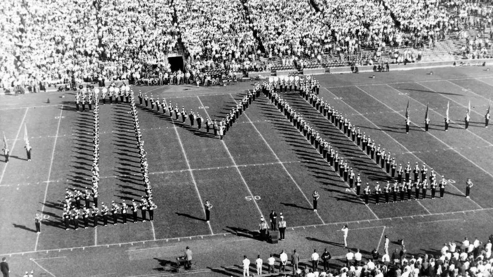 A historic black and white photo of the marching band making the shape of the Block M on the field of the Big House