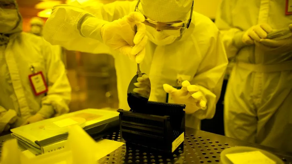 Technicians fully covered in lab gear working inside a semiconductor cleanroom environment