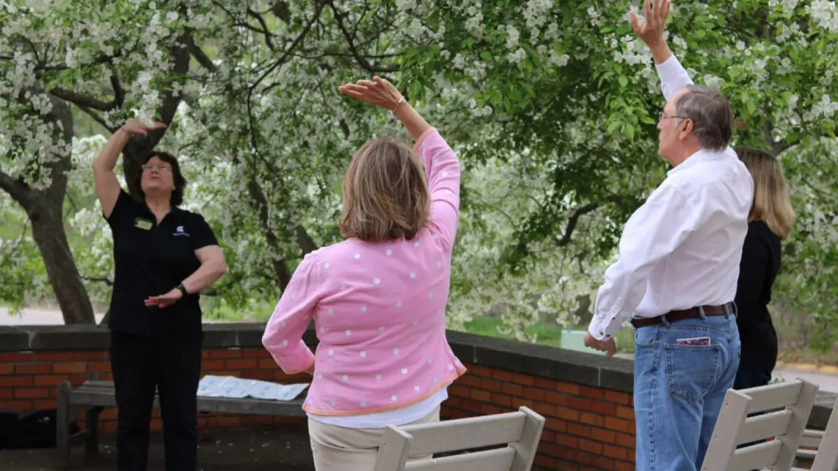 A group of participants practicing tai chi outdoors among blooming trees during a wellness program