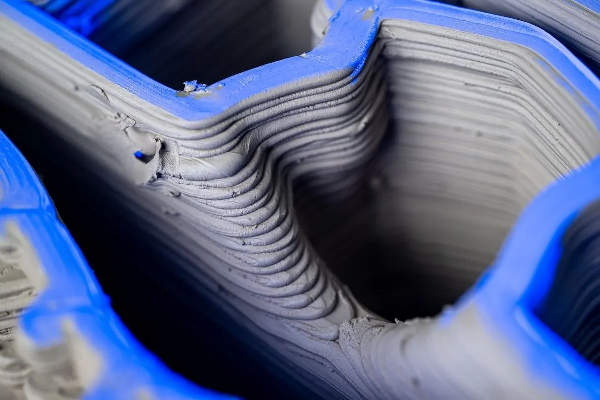 3D-printed concrete layers with wave-pattern ridges inside a blue structural frame